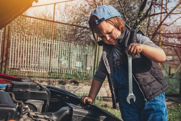 Little child trying to fix broken real car. Dreaming to be auto technician