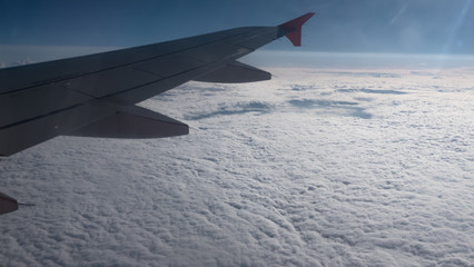 Fototapeta premium Wing of airplane flying above clouds in the sky and with a view thick clouds under sunny rays.