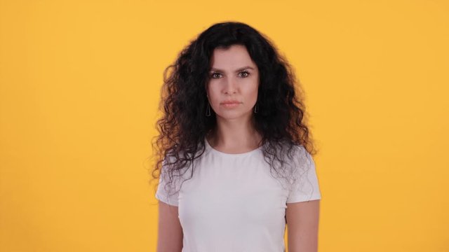 Portrait of beautiful young woman with black curly hair looking strict and gesture a stop sign isolated on yellow background shot in 4k