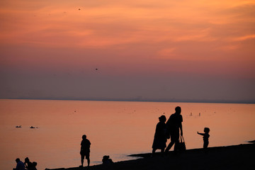 Fototapeta na wymiar Unrecognizable people in silhouette walking on the beach at sunset in Brighton, UK