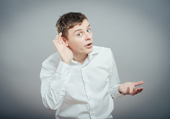 Closeup portrait of handsome young nosy business man secretly listening in on conversation, hand to...