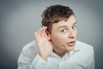 Closeup portrait of handsome young nosy business man secretly listening in on conversation, hand to...