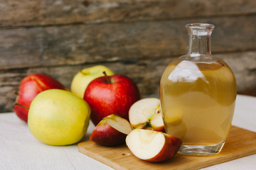 Apple organic vinegar in glass pitcher with ripe fresh red and yellow apples on wooden background. Healthy organic food concept