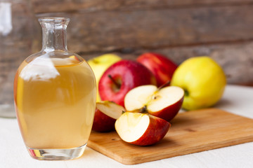 Apple organic vinegar in glass pitcher with ripe fresh red and yellow apples on wooden background. Healthy organic food concept