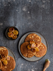 Obraz na płótnie Canvas Oatmeal banana pancakes with honey and babana slices on ceramic plate. Healthy easy making morning breakfast. Homemade sugar free and gluten free food. Concrete background, top view. Copy space.