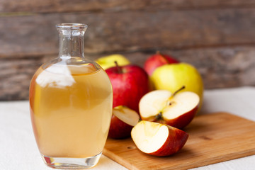 Apple organic vinegar in glass pitcher with ripe fresh red and yellow apples on wooden background. Healthy organic food concept