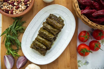 Delicious dolma sarma rice, white yogurt sauce . Garlic, red onion, tarragon . In a stuffed white plate . Yogurt and dried beans in a brown bowl . Red Dry Pepper in Traditional Basket .