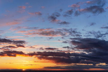 panoramic view of the colorful sky at sunset with the setting sun and orange yellow purple clouds in front of twilight and the last sunbeams