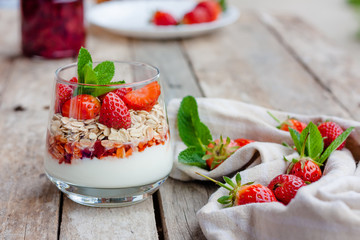 Yogurt with muesli and fresh strawberries for healthy breakfast or snack. Strawberry dessert parfait with yogurt and granola on wooden table. Healthy and organic nutrition. Selective focus
