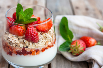 Yogurt with muesli and fresh strawberries for healthy breakfast or snack. Strawberry dessert parfait with yogurt and granola on wooden table. Healthy and organic nutrition. Selective focus