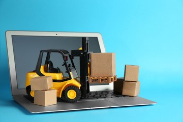 Laptop, forklift model and carton boxes on light blue background. Courier service