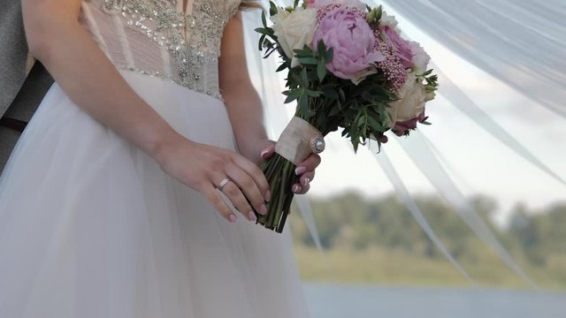 Wedding couple. The groom hugges the bride. Bride and groom embracing outdoors. Man and woman in love. Bride holding her wedding bouquet of peonies and roses.