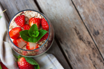 Yogurt with muesli and fresh strawberries for healthy breakfast or snack. Strawberry dessert parfait with yogurt and granola on a wooden table and linen kitchen-towel. top view. selective focus