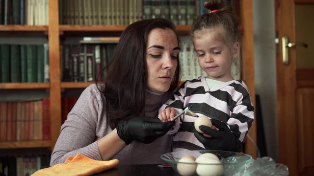 Caucasian mother and little daughter paint Easter eggs in an authentic way with wax candles and paint.