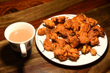 Chai with pakoras and bhajiyas and served on plate on wooden background