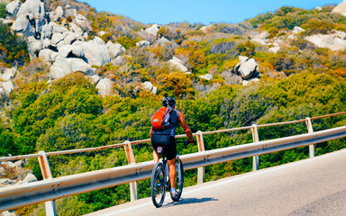 Man riding bicycle on road at rocks at Capo Testa reflex