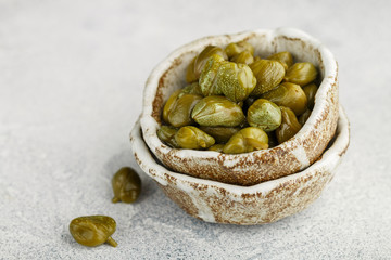 Pickled or salted capers in a ceramic bowl close-up. Unopened flower buds. Delicious ingredients for cooking Mediterranean, Italian, Spanish, French cuisine. Selective focus, copy space