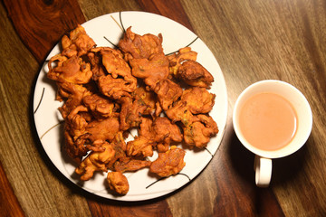 Chai with pakoras and bhajiyas and served on plate on wooden background