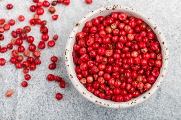 Pink Organic dried Peppercorns in a white bowl on a light concrete or stone background close-up. Spices and seasonings. Selective focus, top view and copy space