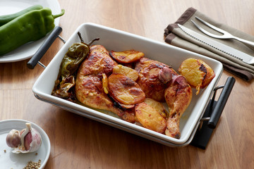 Oven-roasted chicken leg with potatoes and green peppers, served on a white porcelain platter.