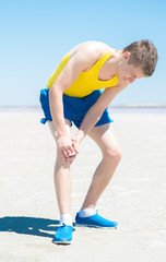 Male athlete on floor clutching knee and hamstring in excruciating pain on white background