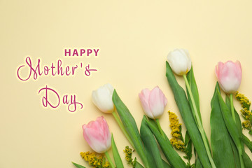 Flat lay composition with beautiful spring flowers and phrase HAPPY MOTHER'S DAY on light yellow background