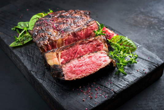 Barbecue Dry Aged Wagyu Entrecote Beef Steak Roast With Lettuce And Salt As Closeup On A Charred Wooden Board