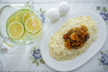 A bowl of white ceramic salt and pepper. Shah pilaf. Khan pilaf in a pita. Black pepper in a white ceramic pot . There is meat and plum chestnuts on the pilaf . Rice in a white plate. Sliced lemon .