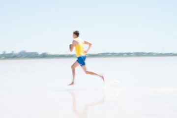 Obraz na płótnie Canvas Young male runner running on a empty beach at dawn. Blur effect.