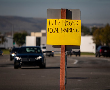 Yellow Handwritten Sign Recruiting For Getting Rich Quick By Flipping Houses At Intersection