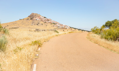 secondary paved road on a summer landscape with a view to Magacela town, province of Badajoz,...