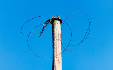 Steel twisted wire on an old wooden pole on a background of blue sky on a sunny day bottom view