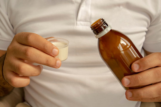 Man in white t-shirt is pouring medical syrup in a measuring cup. Young man holds bottle of syrup with cup. Diarrhea, colitis, dysentery drug.
oral suspension.