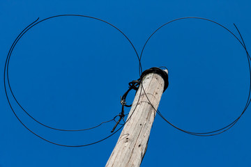 Steel twisted wire on an old wooden pole on a background of blue sky on a sunny day bottom view