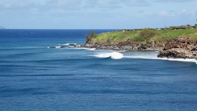 Honolua Bay north of Kapalua on Maui showing a rich blue bay and churning waves rolling across on a sunny Hawaii day where surfers can be seen when the surf is high.