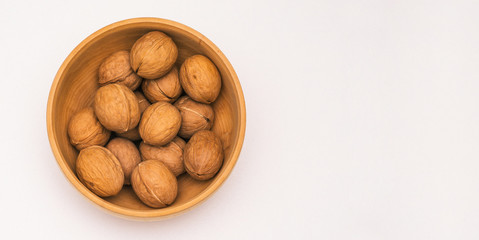 Inshell walnuts lie in a wooden plate. Ripe walnut on a white background. Healthy eating. Top view, copy space.