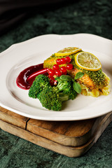 Healthy air fry salmon sprinkled with steamed broccoli, cranberry and sliced lemon in a white plating. Food photography in dark background for cook book concept. - 340068444