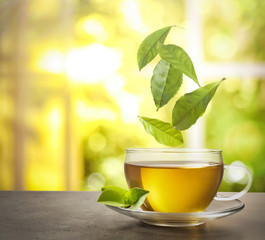 Green leaves falling into cup of tea on table against blurred background. Space for text