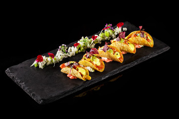 Variety flavors of mini tacos in nice black plating in dark background. Best food presentation for magazine and Mexican cook book. Mexican food plating with flower leaves decoration.