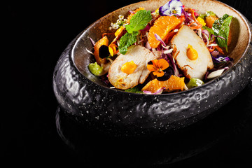 Mexican salad dish with sliced chicken mint leaves orange fresh pulps and flower decoration in black bowl. Food photography perfect for magazine or online delivery menu for restaurants.