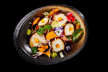 Mexican salad dish with sliced chicken mint leaves orange fresh pulps and flower decoration in black bowl. Appetizer photo in plain background best use for fine dine in restaurant menu.