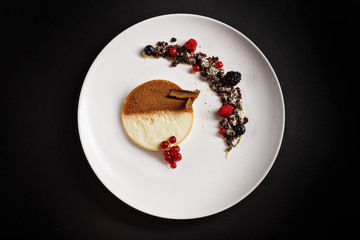 Creme tiramisu tart with cocoa powder on top and  chocolate crumps with berry fruits on the side. Amazing desert plating photography perfect for magazine and fine dine in menu concept.