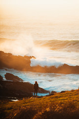Lonely girl watching big waves crash against the rocks