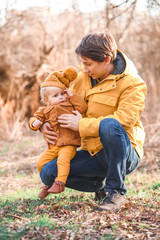 A young father holds his one-year-old son in his arms against a light background and nature.