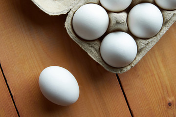 White chicken eggs in a cardboard box and one egg on a wooden table in the top view. Agricultural food products