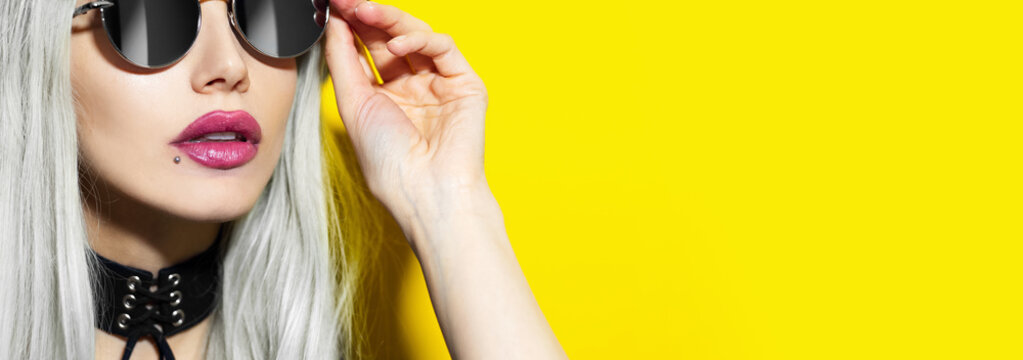 Close-up of studio fashion portrait of young beauty blonde girl wearing sunglasses and black choker on yellow background with copy space.