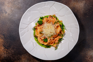 Pasta with chicken, mushrooms and sun-dried tomatoes in a white plate against a dark background. European cuisine. The work of a professional chef. Dish from a restaurant or cafe menu. Top view