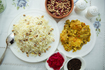 Khan pilaf in a pita . Dry beans on top of pilaf . Dry beans in a brown bowl . Chicken curry on the white plate . red cabbage sauerkraut and black pepper in a small bowl . 