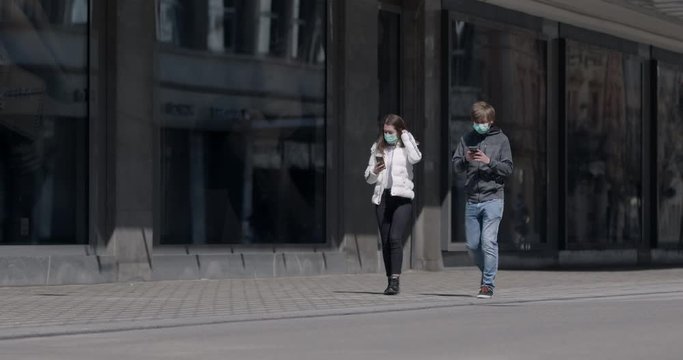 People spending more time online in time of coronavirus pandemic. Two people with medical masks walking side by side and are glued to their phones