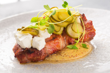 Grilled Pork Steak with Sliced Pickled Cucumber, Sauce and Cheese on White Plate